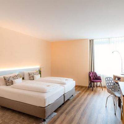 Eines unserer Doppelzimmer.Ein sehr heller, gemütlicher Raum mit Weinrotem Sessel, Weißer Bettwäsche und Graugemusterten Akzentkissen