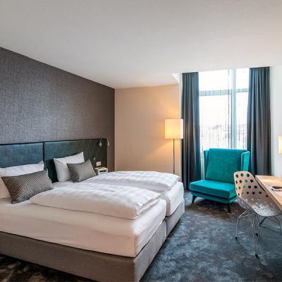 Eines unserer DoppelZimmer mit dunkelgrauer Akzentwand, Türkisenem Backboard und Sessel und weißer Bettwäsche