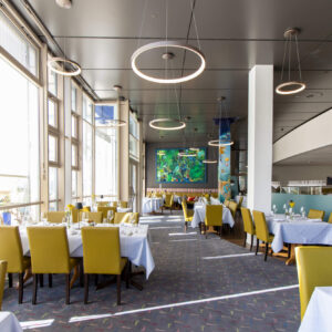 Das untere Restaurant, ein lichtdurchfluteter, offener Raum mit grauen Tischdecken und grünen Stühlen